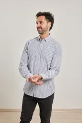Camisa de manga larga confeccionada en tejido de algodón Oxford, con diseño de rayas verticales en tonos gris y blanco, cuello abotonado y bolsillo frontal.