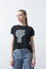 Remera negra de manga corta con puños doblados, cuello redondo y estampado frontal de un jarrón con flores blancas.