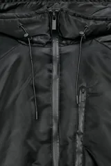 Chaqueta acolchada de color negro con acabado repelente al agua y resistente al viento. Presenta cuello subido con capucha ajustable, cierre frontal con cremallera termosellada, bolsillos delanteros con cremallera y bajo con ajuste elástico. Las mangas largas cuentan con tiras adhesivas ajustables en los puños.