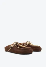 Zueco de gamuza marrón, estilo slip-on, con cordones frontales decorativos, abalorios y suela plana.