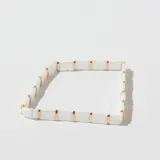 Pulsera elástica con cuentas rectangulares de color blanco y separadores dorados.