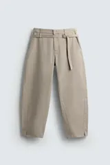 Pantalón de algodón color beige, estilo wide balloon fit, con cintura ajustable mediante cinturón de la misma tela. Presenta bolsillos frontales y bolsillos traseros de plastrón, con efecto lavado y abertura en el bajo.