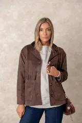 Chaqueta de gamuza sintética color marrón, con diseño de flecos en el pecho y la espalda. Presenta cierre frontal con botones, cuello camisero y bolsillos cuadrados frontales.