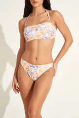 Conjunto de bikini con estampado tropical de frutas y hojas en tonos naranja, amarillo y violeta. El corpiño es tipo bandeau con tirante halter ajustable, y la bombacha es de corte colaless.