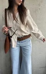 Camisa de manga larga color beige con detalles de encaje y calados verticales en el frente y las mangas, cuello en V y cierre frontal con botones.