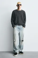 Zapatilla de piel color negro con acabado serraje, cordonera oculta y suela plana a contraste en color crema.