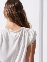 Remera blanca de modal, marca French Laundry, con escote en V. Presenta apliques de puntilla en las mangas y el escote, y un detalle fruncido en los hombros.