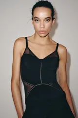 Body de escote corazón con aros y tirantes finos ajustables. Presenta un diseño con paneles de tejido opaco y transparencias laterales. Cierre inferior con botones a presión.