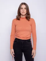 Polera color salmón de textura acanalada, cuello alto y mangas largas con ajuste fruncido en los laterales.