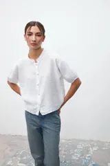 Camisa blanca de lino con cuello mao, manga corta y cierre frontal con botones.