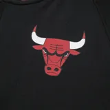 Campera negra con detalles en rojo y blanco, con cierre frontal y bolsillos laterales. Presenta el logo de los Chicago Bulls en el pecho y letras en el brazo izquierdo.