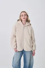 Campera de corderito con capucha, cierre frontal completo y bolsillos laterales. Presenta un diseño holgado de manga larga en color beige.