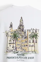 Remera blanca de punto de algodón, con cuello redondo y hombros caídos, corte holgado. Presenta un pequeño estampado en el pecho con el texto "MENTON FRANCE" en color oscuro.
