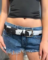 Cinturón de cuero con textura de pelo y estampado de manchas tipo vaca en blanco y negro, con hebilla metálica plateada.