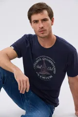 Remera azul marino de manga corta con cuello redondo, confeccionada en mezcla de algodón y poliéster. Presenta un estampado frontal circular de inspiración vintage con diseño de velero y tipografía alusiva a clubes deportivos.