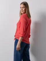 Blusa blanca de gasa marca Zac & Rachel, con cuello a la base, escote en V, abertura central con botones, bolsillo aplicado en el pecho y mangas largas regulables con presilla y botón. Tiene terminación opcional de nudo en el ruedo.