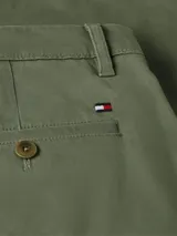 Pantalón chino cónico color verde militar, confeccionado en satén de algodón elástico. Cuenta con cierre de cremallera y botón, dos bolsillos laterales abiertos, pequeño bolsillo delantero en la cintura y dos bolsillos traseros de ojal con botón.