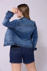 Campera de jean azul de lavado medio, con cuello tradicional, botones metálicos marrones, bolsillos superiores con tapa y puños abotonados.
