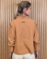 Blusa blanca de algodón con escote en V y cuello mao. Presenta mangas largas abullonadas con puños acampanados y fruncidos.
