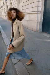 Chaqueta de corte recto y estilo camisero en color beige, con cuello solapa, manga larga y cierre frontal con botones. Presenta dos bolsillos delanteros de plastrón.