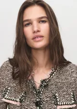Chaqueta de tweed con diseño recto y cuello redondo. Presenta cierre frontal con botones, manga larga y cuatro bolsillos de solapa en la parte delantera. Destaca por sus terminaciones deshilachadas y ribetes en contraste.
