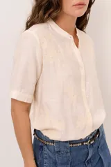 Camisa de manga corta color blanco con cuello mao y cierre frontal de botones. Presenta detalles bordados tono sobre tono en el canesú y diseño de corte recto.