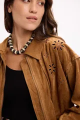 Campera de gamuza color beige con diseño de calados florales en hombros y espalda, cierre frontal y cuello camisero. Presenta un corte relajado y textura suave.