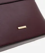 Cartera bandolera pequeña de formato rectangular, confeccionada en poliuretano con acabado liso. Presenta una correa larga ajustable, cierre superior con cremallera y un pequeño aplique metálico dorado con el logo de la marca en el frente.