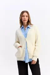 Saco de punto color crema con escote en V, cierre frontal con botones y bolsillos delanteros. Presenta un diseño de calce relajado con estructura marcada.