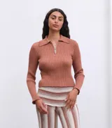 Buzo tejido de punto acanalado en color terracota, con cuello polo y cierre frontal parcial. Presenta mangas largas con terminación acampanada y ajuste al cuerpo.