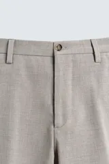 Pantalón de vestir slim fit en color beige, confeccionado en tejido con lana. Presenta cierre frontal con cremallera y botón, bolsillos laterales y bolsillos traseros de doble vivo con botón.