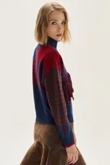 Polera de tejido de punto con diseño multicolor que combina rayas horizontales en tonos azul y bordó, flecos decorativos en el frente y un bordado central en forma de trenza. Presenta cuello semi polera, mangas largas y puños acanalados.