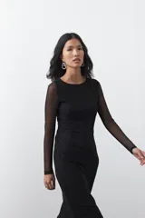 Vestido largo de manga larga confeccionado en tejido de malla transparente con sutil textura. Presenta un diseño entallado, cuello redondo y una silueta estilizada.