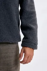 Buzo de sherpa en color gris oscuro, con cuello alto y cierre frontal parcial. Presenta un bolsillo frontal con cierre y diseño de manga larga.