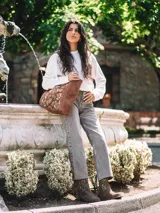 Bolso tipo tote bag confeccionado en cuero serraje color marrón, con diseño artesanal que incluye bordados florales coloridos en el panel frontal. Cuenta con asas de hombro y cierre superior.
