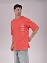 Remera de corte oversize color naranja, con cuello redondo y mangas cortas. Presenta un estampado gráfico minimalista en el pecho que incluye un globo terráqueo y texto.