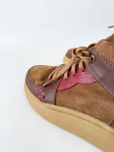 Zapatillas acordonadas de cuero marrón con detalles en rojo y suela de goma color caramelo.