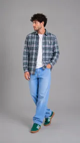 Camisa de manga larga con diseño de cuadros escoceses en tonos gris, verde y blanco. Presenta cuello clásico, cierre frontal con botones y un pequeño bordado distintivo en el pecho.