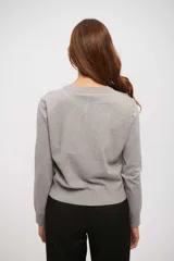 Saco de tejido de punto gris claro, de manga larga y cuello redondo, con cierre frontal de botones pequeños.