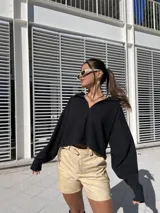 Buzo de punto color negro con cuello polo abierto, mangas largas amplias y corte cropped de silueta relajada.