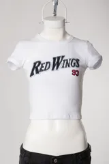 Remera tipo baby tee blanca de manga corta, con cuello redondo y diseño ajustado al cuerpo con estampado y bordado frontal "Red Wings 93".