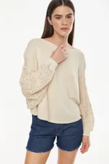 Sweater de punto liviano color crudo, con cuello bote, mangas largas abullonadas con diseño calado y corte cropped.