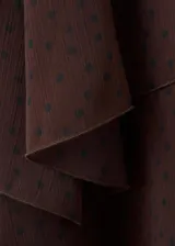 Vestido corto marrón con estampado de lunares, cuello alto y diseño de capas superpuestas con volados. Mangas largas abullonadas semitransparentes.