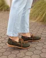 Zapatos náuticos de cuero verde oscuro, estilo mocasín con cordones de cuero marrón claro, costuras visibles en contraste y suela plana.