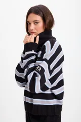 Campera holgada de tejido de punto con cuello alto tipo chomba y cierre frontal oculto. Presenta un diseño de rayas horizontales en negro, gris y celeste, con detalle de bordado en la manga.