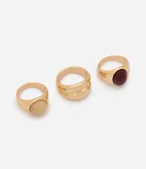 Kit de tres anillos dorados de estructura robusta, acabado pulido y detalles de resina en tonos beige y burdeo.