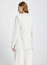 Saco largo tejido color blanco con textura en relieve, corte recto, cuello semi alto, mangas largas y ribete de flecos en el dobladillo, los puños y el cuello.