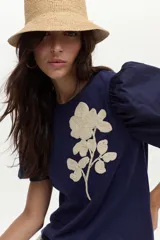 Blusa azul marino de algodón, con mangas abullonadas cortas de tela plana y gran bordado de rosa en tono crudo en el pecho.