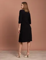 Vestido midi negro de RM Richards en seda fría, con escote en V, mangas 3/4, frunce en la delantera y aplique circular de brillos en el centro.