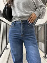 Pantalón de jean azul con corte recto y tiro alto, presenta detalles de tachas metálicas en los bolsillos delanteros.